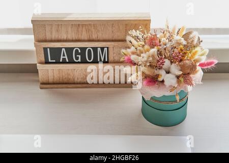 Beau bouquet de fleurs séchées et panneau en bois avec texte LAGOM sur table blanche Banque D'Images