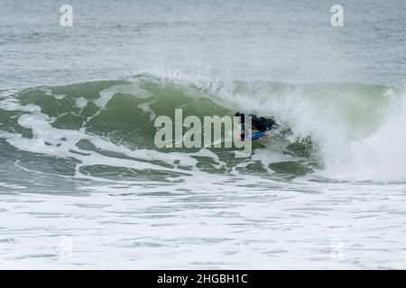 Bodyboarder effectuant un tour de tube surf océan ondulant vague de l'océan sur une journée d'hiver nuageux. Banque D'Images