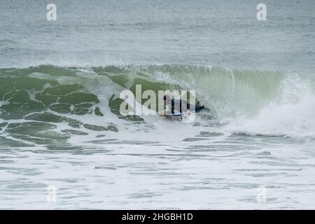 Bodyboarder effectuant un tour de tube surf océan ondulant vague de l'océan sur une journée d'hiver nuageux. Banque D'Images