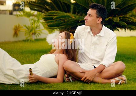 Une femme et un homme de singe.Couple en vacances, sous un palmier.Repos, tabagisme, nicotine, plaisir, danger.Liquide VAPE.Vaping THC e cigarette. Banque D'Images