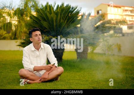 Un homme de vape en vacances, sous un palmier.Repos, tabagisme, nicotine, plaisir, danger.Liquide VAPE.Vaping THC e cigarette. Banque D'Images