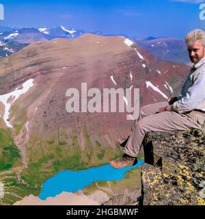 autoportrait de john lambing assis sur le bord de la tête du mont siyeh au-dessus du lac cracker dans le parc national du glacier, montana Banque D'Images