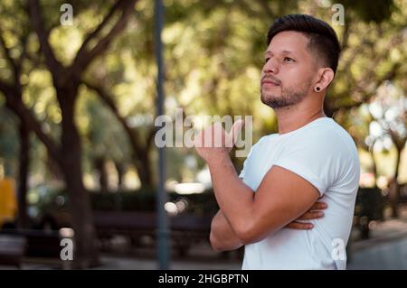 Beau jeune homme, hispano-latin, avec barbe et cheveux courts, vêtu d'un flanelle blanc, est debout avec ses bras croisés et regarde pensive dans un Banque D'Images