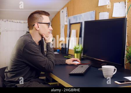 L'homme en lunettes utilise le clavier et la souris regarde l'écran vert.Un homme travaille à la maison.Restez à la maison, indépendant, joueur. Banque D'Images