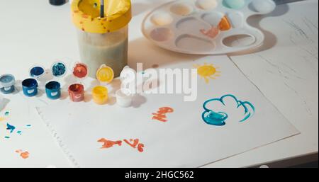 Feuille de papier avec dessin d'un enfant et peinture sur une table blanche Banque D'Images