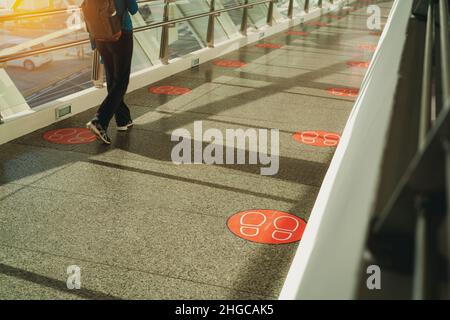 Vue arrière de la femme marchant sur le pont de verre piétonnier.Liaisons par couloir entre les bâtiments avec des symboles sociaux de distance sur le sol pour la distance Banque D'Images