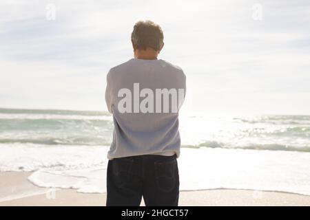 Vue arrière de l'homme biracial senior debout sur la rive regardant l'horizon au-dessus de la mer pendant la journée ensoleillée Banque D'Images