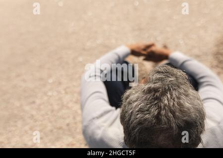 Vue en grand angle de l'homme aîné biracial avec des cheveux gris assis à la plage le jour ensoleillé Banque D'Images