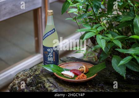 Set de sushi et sashimi avec saké servi sur pierre grise avec jardin en arrière-plan. Banque D'Images