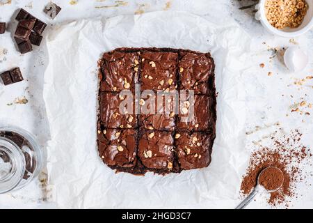 Brownies au caramel au chocolat avec chapelure de noisette sur le dessus, sur un plateau avec de la poudre de cacao, chapelure de chocolat sur un fond rustique blanc. Banque D'Images