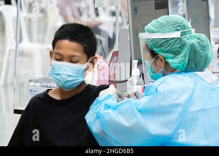 Bangkok, Thaïlande - 25 janvier 2022 : médecin asiatique injectant la vaccination antivirale contre le covid dans le bras du garçon avec masque facial protecteur. Banque D'Images