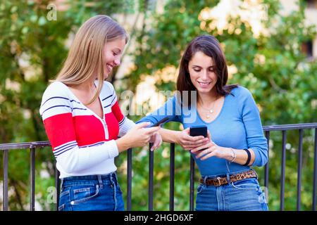 Deux belles jeunes femmes et meilleurs amis souriant tout en utilisant leur téléphone mobile pour s'amuser et les médias sociaux en plein air Banque D'Images