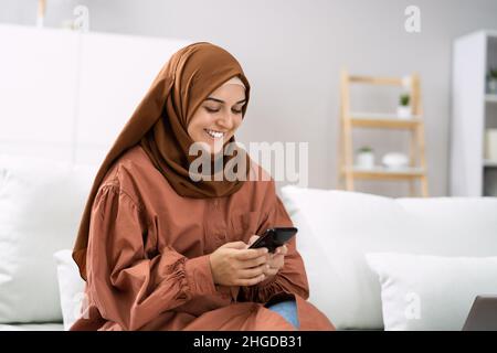 Jeune femme heureuse utilisant un téléphone portable assis sur un canapé Banque D'Images