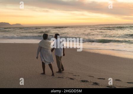 Une longue longueur de couple biracial senior marchant ensemble sur la plage pendant le coucher du soleil Banque D'Images