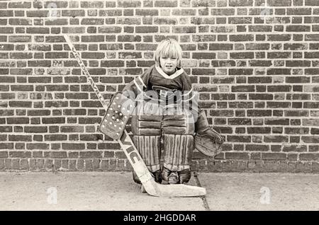 Portrait posé d'un jeune lad qui joue le gardien de but d'une équipe de hockey de rue de patin à roulettes.À Brooklyn, New York, vers 1975. Banque D'Images