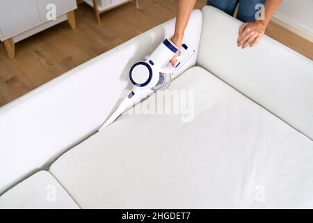 Jeune femme en train de nettoyer le canapé avec aspirateur sans