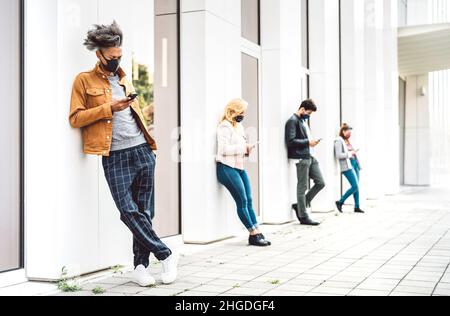 Les personnes utilisant des téléphones cellulaires couverts de masque à la variante d'onde omicron - ennuient des hommes et des femmes à la recherche de nouvelles sur les appareils mobiles Banque D'Images