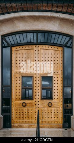 Un gros plan vertical de portes massives en bois avec un motif de rivets en métal sur elle, des portes-fenêtres en acier, et deux fenêtres transparentes au milieu Banque D'Images