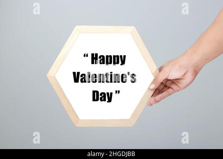 Mains pour hommes avec cadre hexagonal inscrit Happy Valentine's Day dans un style minimaliste féminin fond en lin gris doux - parfait pour la Saint-Valentin D. Banque D'Images