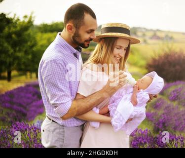 Bonne famille de race blanche mère, père et fille portent des vêtements blancs ont du plaisir dans le champ de lavande.Un couple allaite un bébé à partir d'un biberon Banque D'Images