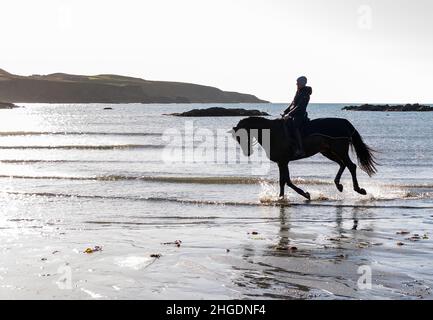 Silhouette de femme à cheval à travers les vagues sur la plage.West Cork Irlande Banque D'Images