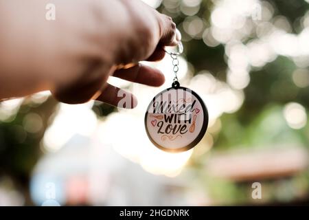 La main d'un homme tient un porte-clés rond avec les mots Mixed with Love sur un fond doux de lumière du soleil couchant. Banque D'Images