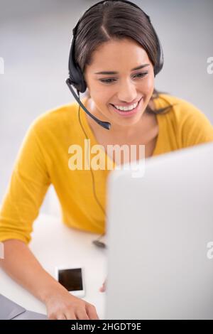 Aider ses clients avec finesse.Photo d'un jeune représentant du service clientèle portant un casque tout en étant assis près de son ordinateur. Banque D'Images