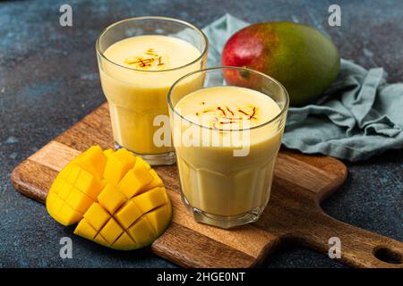 Buvez du lassi de mangue dans deux verres sur une table en béton rustique avec du manfo frais et mûr coupé par le dessus Banque D'Images