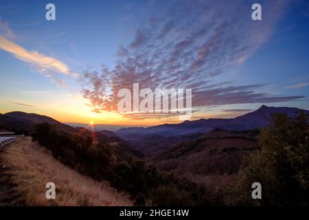 Soleil orange brillant à l'horizon sur un paysage de lever de soleil depuis le sommet d'une montagne avec quelques beaux nuages rouges de cirrus dans le ciel Banque D'Images