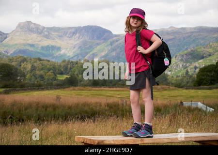 jeune fille de 7 ans en vêtements de randonnée debout sur une plate-forme dans le district de langdale valley lake, cumbria, angleterre, royaume-uni Banque D'Images