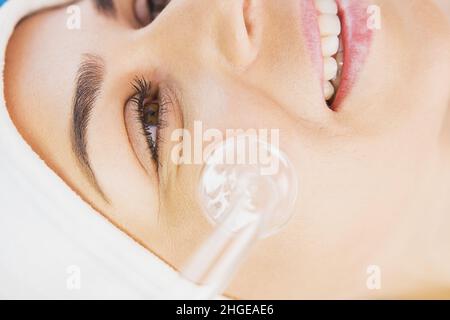 Gros plan d'une femme souriante et heureuse bénéficiant d'un massage du visage sous vide, recevant un massage électrique de la procédure darsonval au salon de beauté.Matériel Banque D'Images