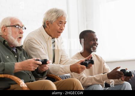 KIEV, UKRAINE - 12 OCTOBRE 2021: Des hommes seniors multiethniques concentrés jouant au jeu vidéo à la maison Banque D'Images