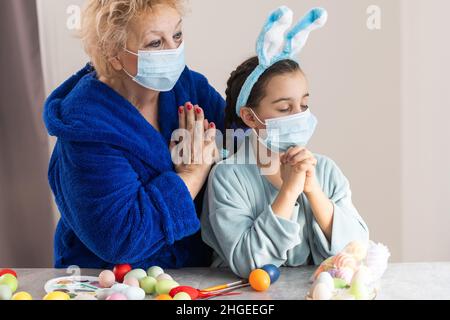 la grand-mère et les enfants peignent des œufs.Une famille heureuse se prépare pour Pâques.Petites filles mignonnes portant des oreilles de lapin. Banque D'Images