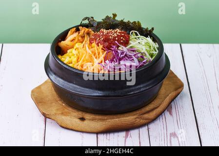 Riz alimentaire coréen bibimbap avec légumes, boeuf et teriyaki dans un bol noir sur fond de balle de bois Banque D'Images