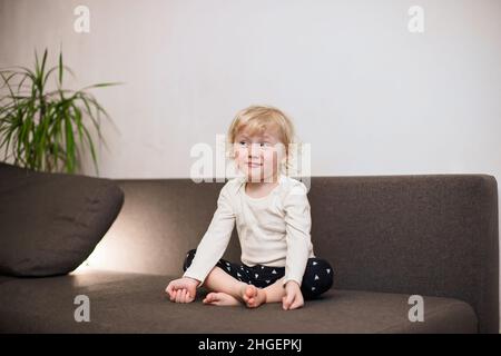 Petite fille mignonne méditant sur le canapé à la maison.Enfant faisant de l'exercice de yoga dans la pose de lotus près de chat Banque D'Images