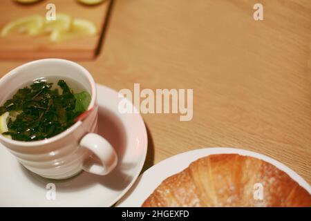 Menthe dans une casserole sur le fond d'une tasse de thé.Croissants et citrons en arrière-plan.Thé vert, goût de thé maison. Banque D'Images