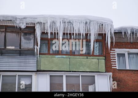 Balcons d'une ancienne maison résidentielle en brique couverte par les immenses glaçons.Des glaçons dangereux pendent du toit.Difficile nord hiver dans la ville. Banque D'Images