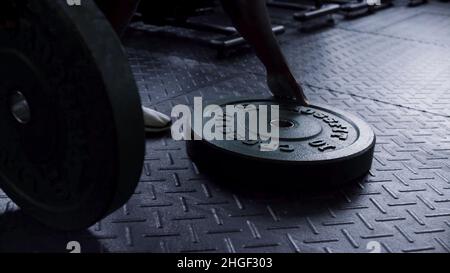 Gros plan pour les assiettes lourdes sur le sol de la salle de gym prêt à être utilisé par un homme pour l'entraînement de force.Homme prenant l'équipement d'exercice de forme physique poids de barbell Banque D'Images