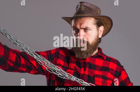 Homme sérieux en chemise à carreaux avec chaîne en métal.Mâle barbu en chapeau avec chaînes en acier.Liberté. Banque D'Images