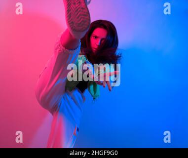 La brunette danse au néon, la danseuse en rouge-bleu.Hip hop fille, fête, sourire.Modèle en vol, saut.Photo lumineuse, émotions. Banque D'Images