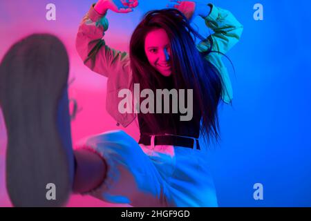 La brunette danse au néon, la danseuse en rouge-bleu.Hip hop fille, fête, sourire.Modèle en vol, saut.Photo lumineuse, émotions. Banque D'Images