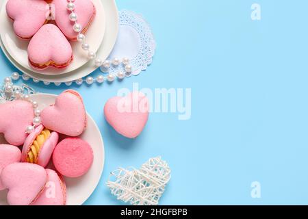 Composition avec de savoureux macarons en forme de coeur et des perles sur fond bleu Banque D'Images