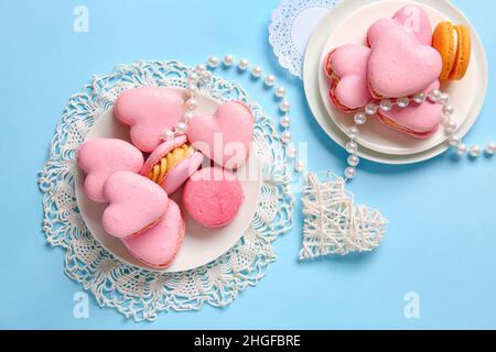 Composition avec de savoureux macarons en forme de coeur et des perles sur fond bleu Banque D'Images