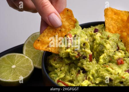 Gros plan de la main de femme avec une puce de tortilla ou des nachos avec une délicieuse sauce guacamole Banque D'Images