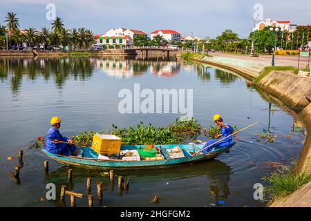 Deux hommes en combinaison bleue nettoyant l'eau dans la vieille ville dans un bateau de 2 hommes. Banque D'Images