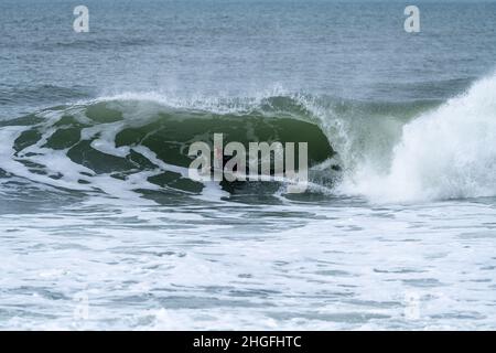 Bodyboarder effectuant un tour de tube surf océan ondulant vague de l'océan sur une journée d'hiver nuageux. Banque D'Images