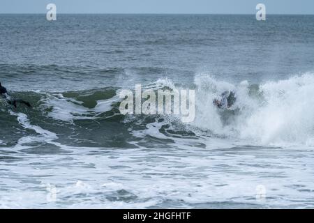 Bodyboarder effectuant un tour de tube surf océan ondulant vague de l'océan sur une journée d'hiver nuageux. Banque D'Images