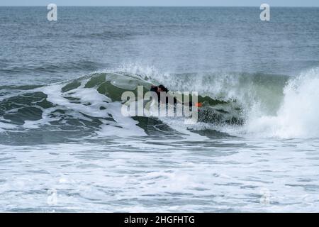 Bodyboarder effectuant un tour de tube surf océan ondulant vague de l'océan sur une journée d'hiver nuageux. Banque D'Images