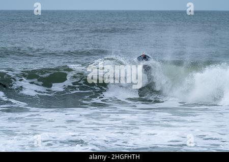 Bodyboarder effectuant un tour de tube surf océan ondulant vague de l'océan sur une journée d'hiver nuageux. Banque D'Images