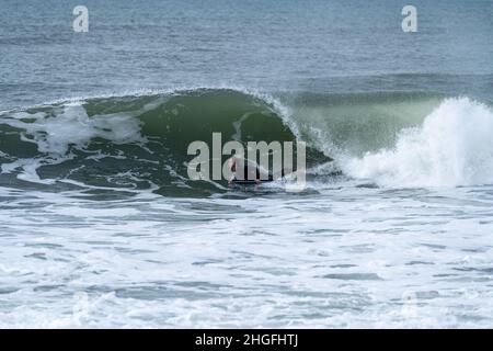 Bodyboarder effectuant un tour de tube surf océan ondulant vague de l'océan sur une journée d'hiver nuageux. Banque D'Images